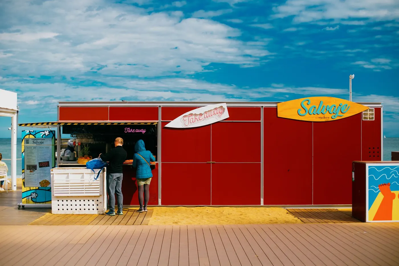 A bright beach kiosk on a boardwalk under a blue sky